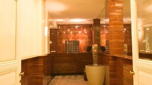 Un vestíbulo de hotel con un mostrador de recepción, un jarrón grande con flores y una alfombra estampada.