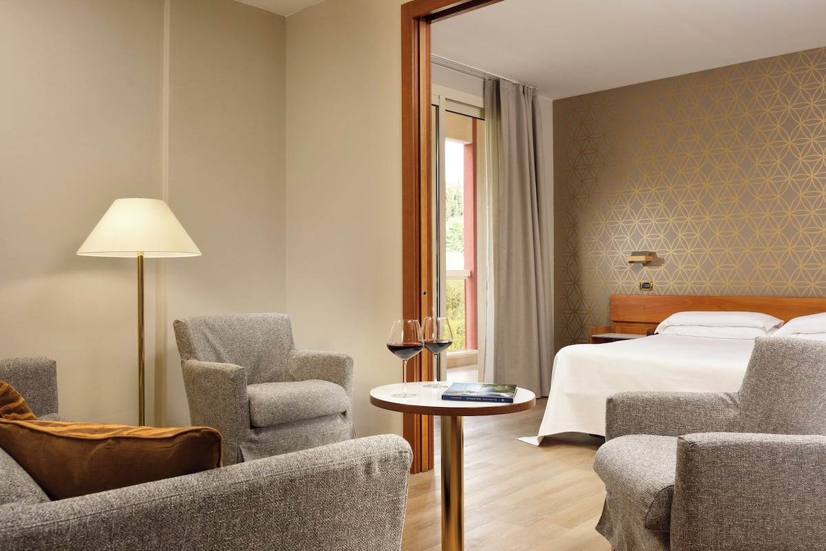 Una habitación de hotel con cama, dos sillones, una mesita y una lámpara de pie.