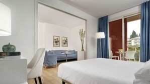 Habitación de hotel con cama, escritorio, silla, sofá, una mesita y vistas al exterior.