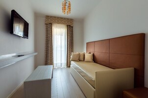 Camera d'albergo con un letto, una TV a muro, un tavolino e una finestra con tende.