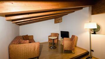 Una habitación acogedora con techo de madera, un sofá, dos sillones estampados, una mesita redonda pequeña, un televisor y una lámpara de pie.