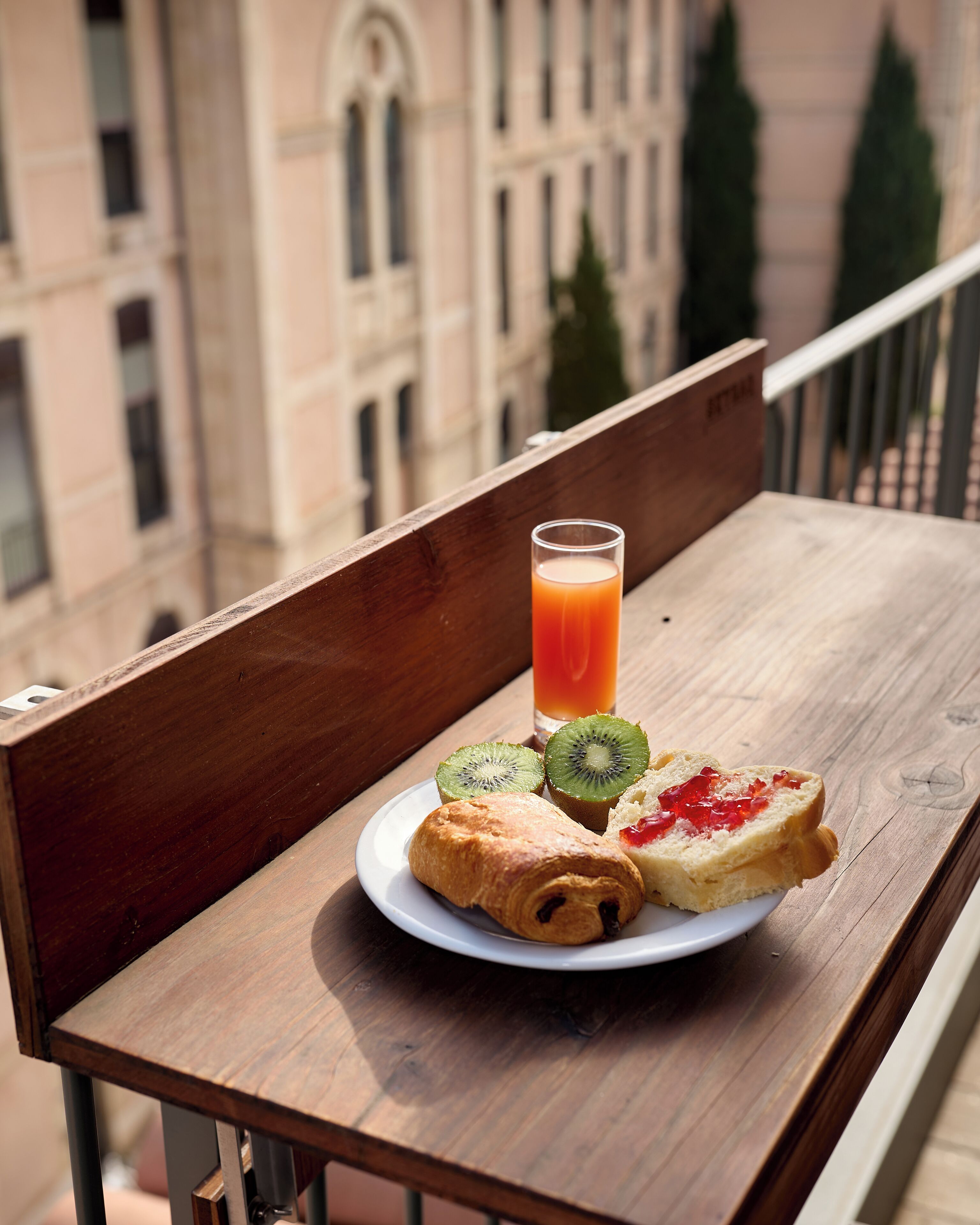 Una mesa de madera con un plato de comida y un vaso de jugo de naranja en un balcón.