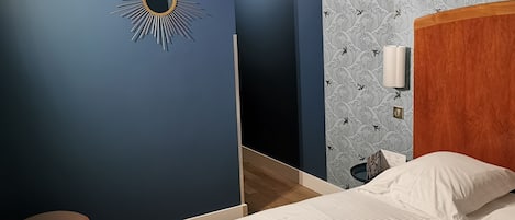 A hotel room with a bed, a nightstand, a wall-mounted lamp, and a chair.