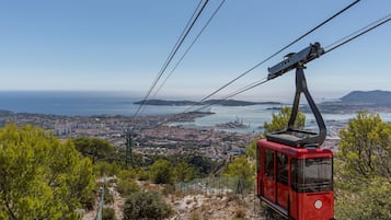 A cable car system with a red gondola, a clear view of a coastal cityscape, and a body of water in the distance.