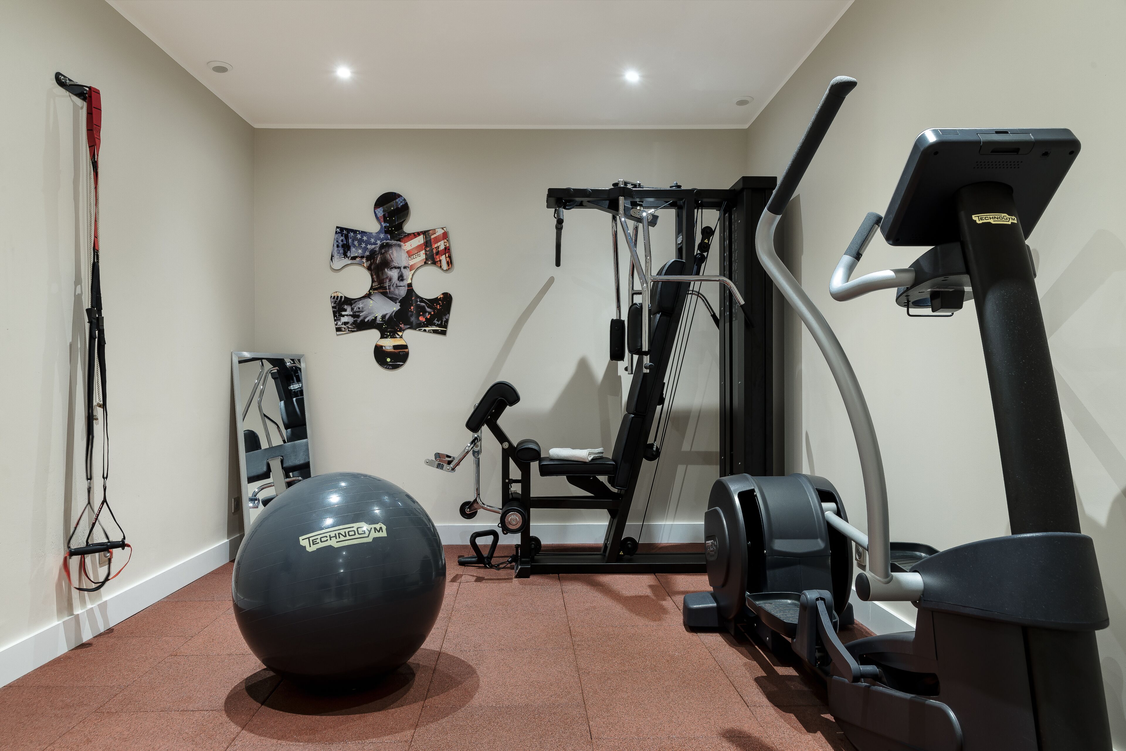 Un gimnasio en casa con cinta de correr, elíptica, banco de pesas y pelota de ejercicios.