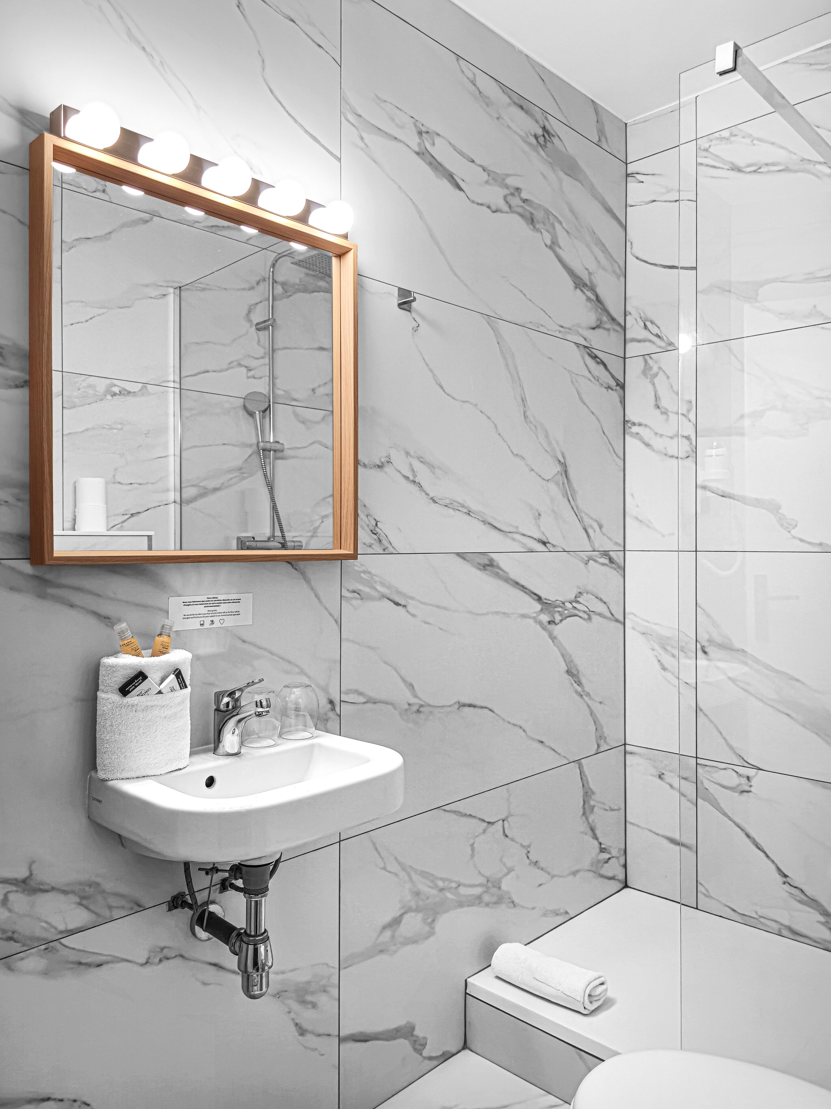Un baño moderno con salpicadero de mármol, tocador con espejo e iluminación, ducha y retrete.