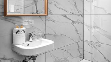 Un baño moderno con salpicadero de mármol, tocador con espejo e iluminación, ducha y retrete.