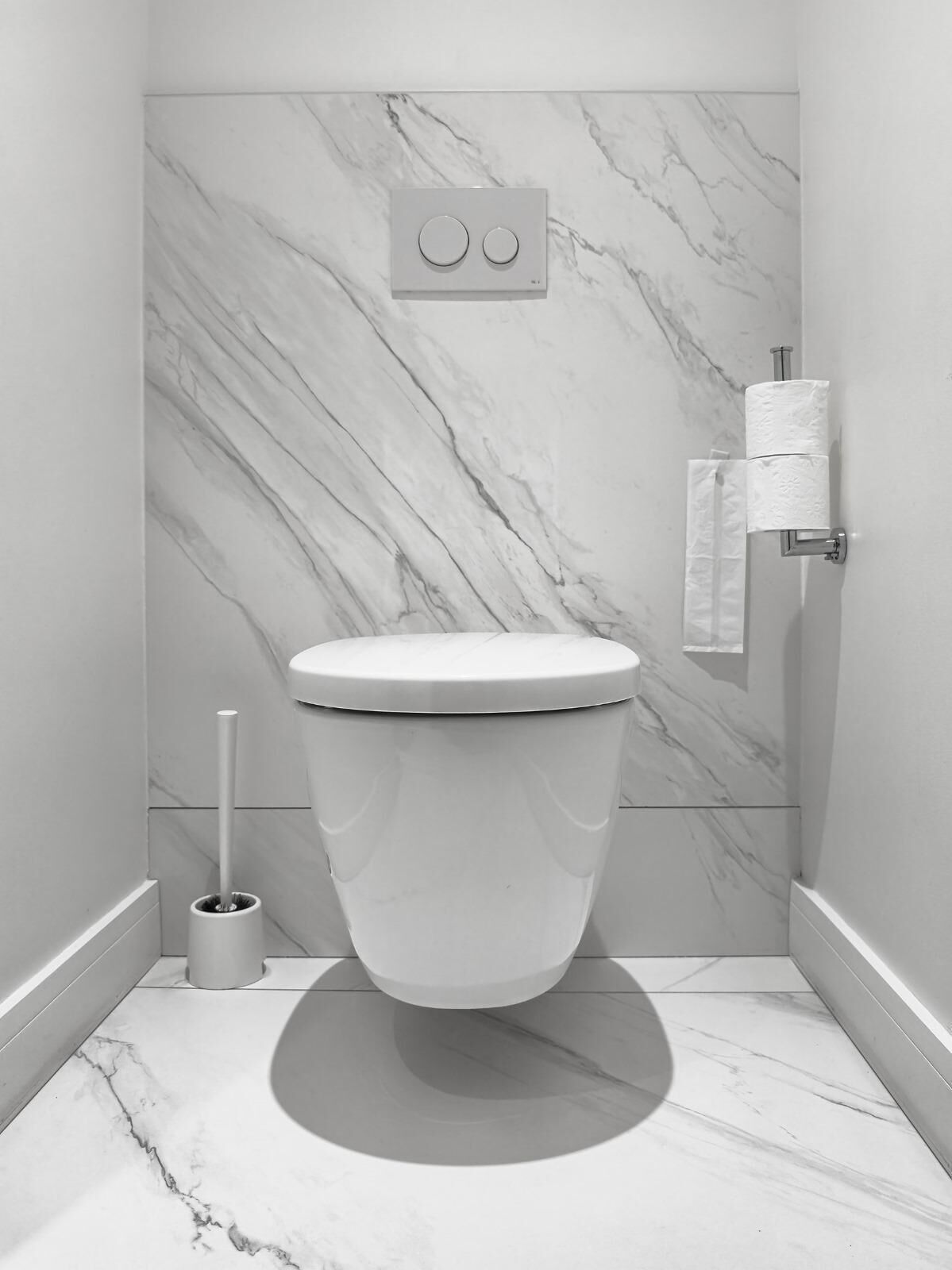 Un baño moderno con inodoro, paredes de mármol y un dispensador de papel higiénico.