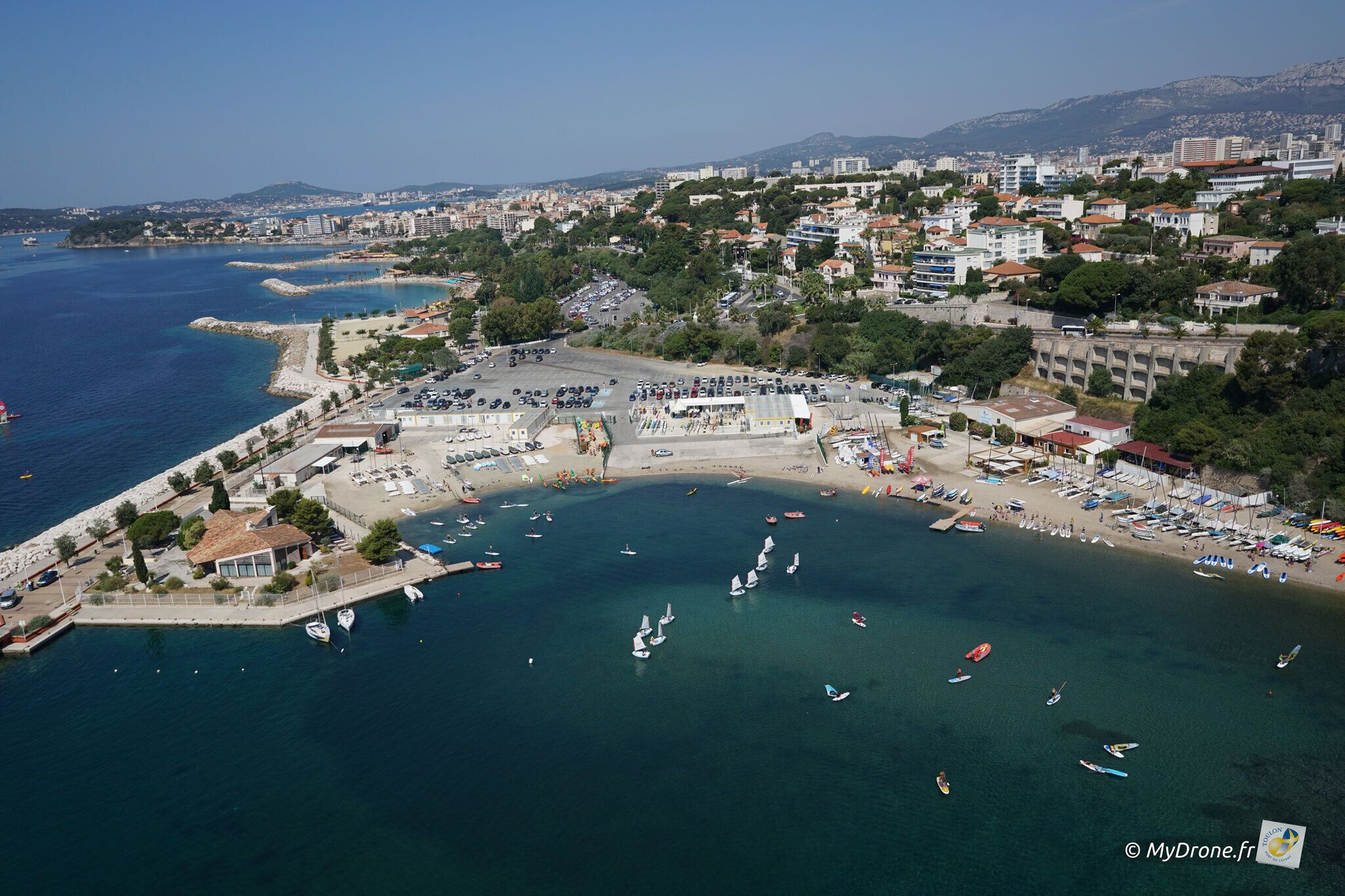 An aerial view of a coastal town with a marina, beach, and residential buildings.