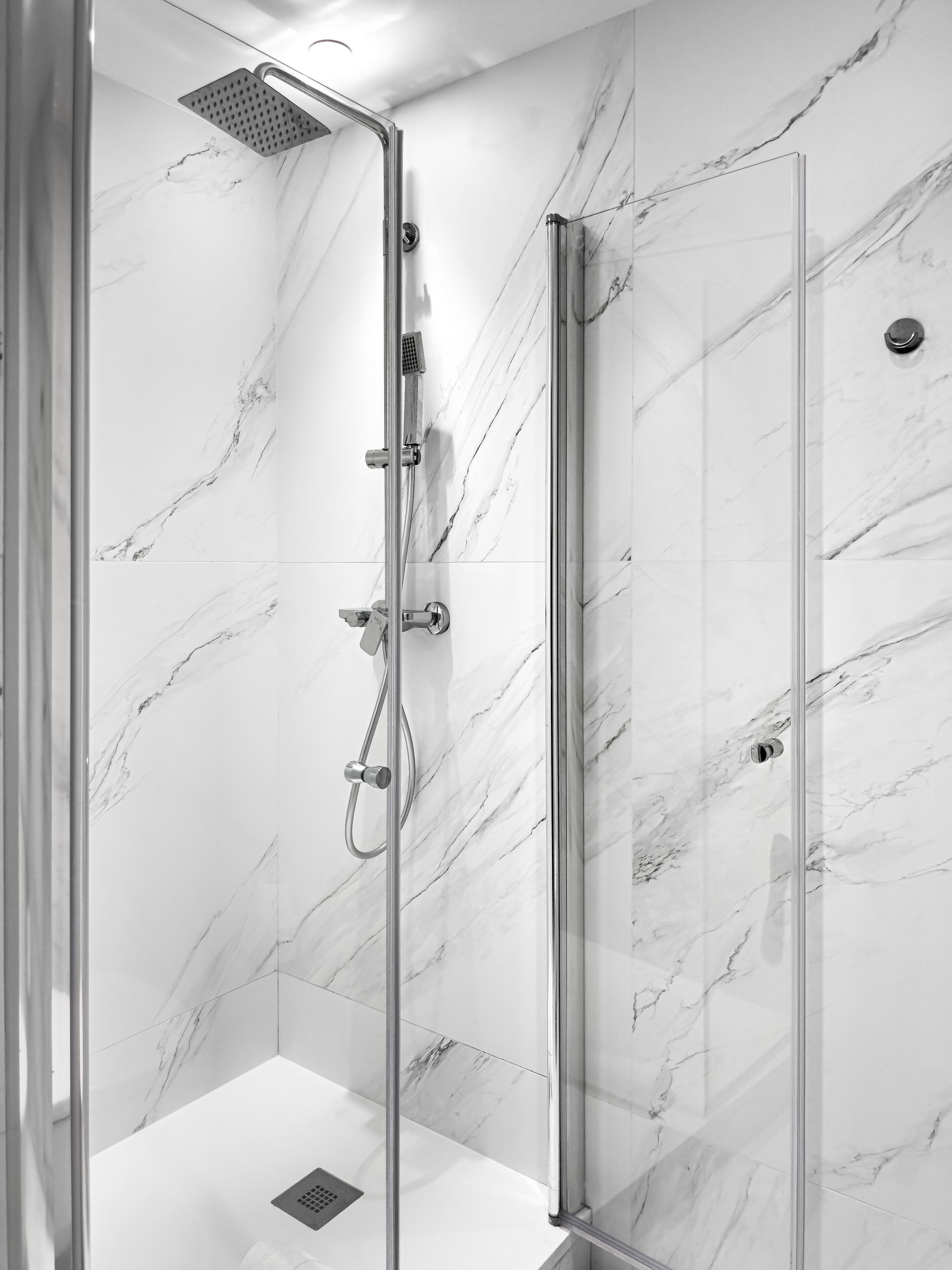 A modern shower with a glass door, marble walls, and a handheld showerhead.