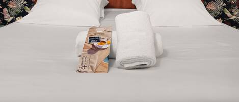 Habitación de hotel con papel tapiz floral, cabecera de madera, ropa de cama blanca y una toalla sobre la cama.