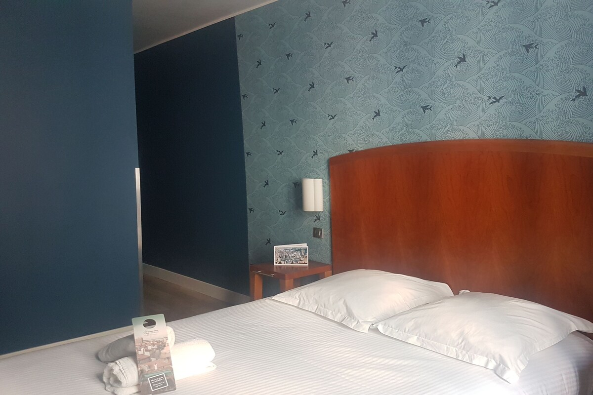 A hotel room with a bed, a nightstand, a wall-mounted lamp, and a patterned wallpaper.
