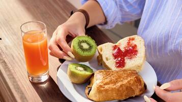 Un plato de desayuno con tostadas, mermelada y rodajas de kiwi, además de un vaso de jugo de naranja sobre una mesa de madera.