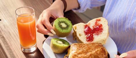 A breakfast plate with toast, jam, and kiwi slices, and a glass of orange juice on a wooden table.