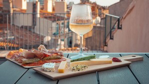 A table with a glass of white wine, a charcuterie board with various cheeses, meats, and pickles, and a cityscape in the background. - Grand Hôtel Dauphiné Toulon, Boutique Hôtel & Suites (Toulon)