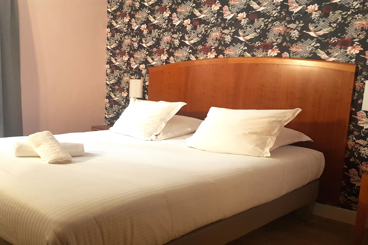 Una cama bien tendida con sábanas y almohadas blancas, cabecera de madera y papel tapiz floral.