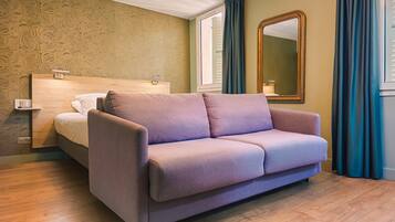 A room with a purple sofa, a wooden headboard bed, a large mirror, and a patterned wallpaper.