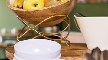 Un saladier en bois contenant des fruits, posé sur un présentoir, avec des assiettes blanches et des cuillères sur une table en bois.
