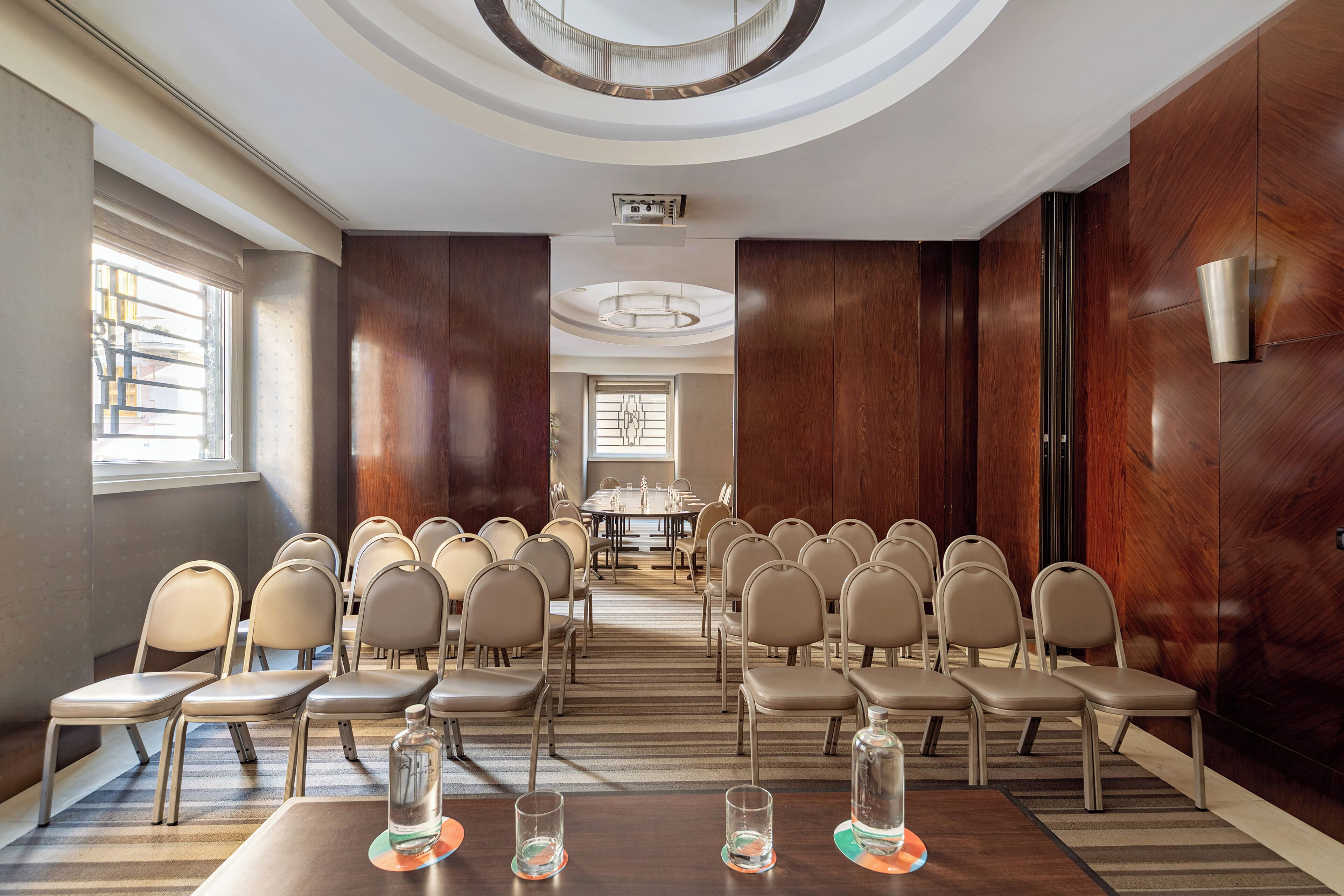 Un salón de conferencias con filas de sillas, una mesa larga y un diseño moderno en el techo.