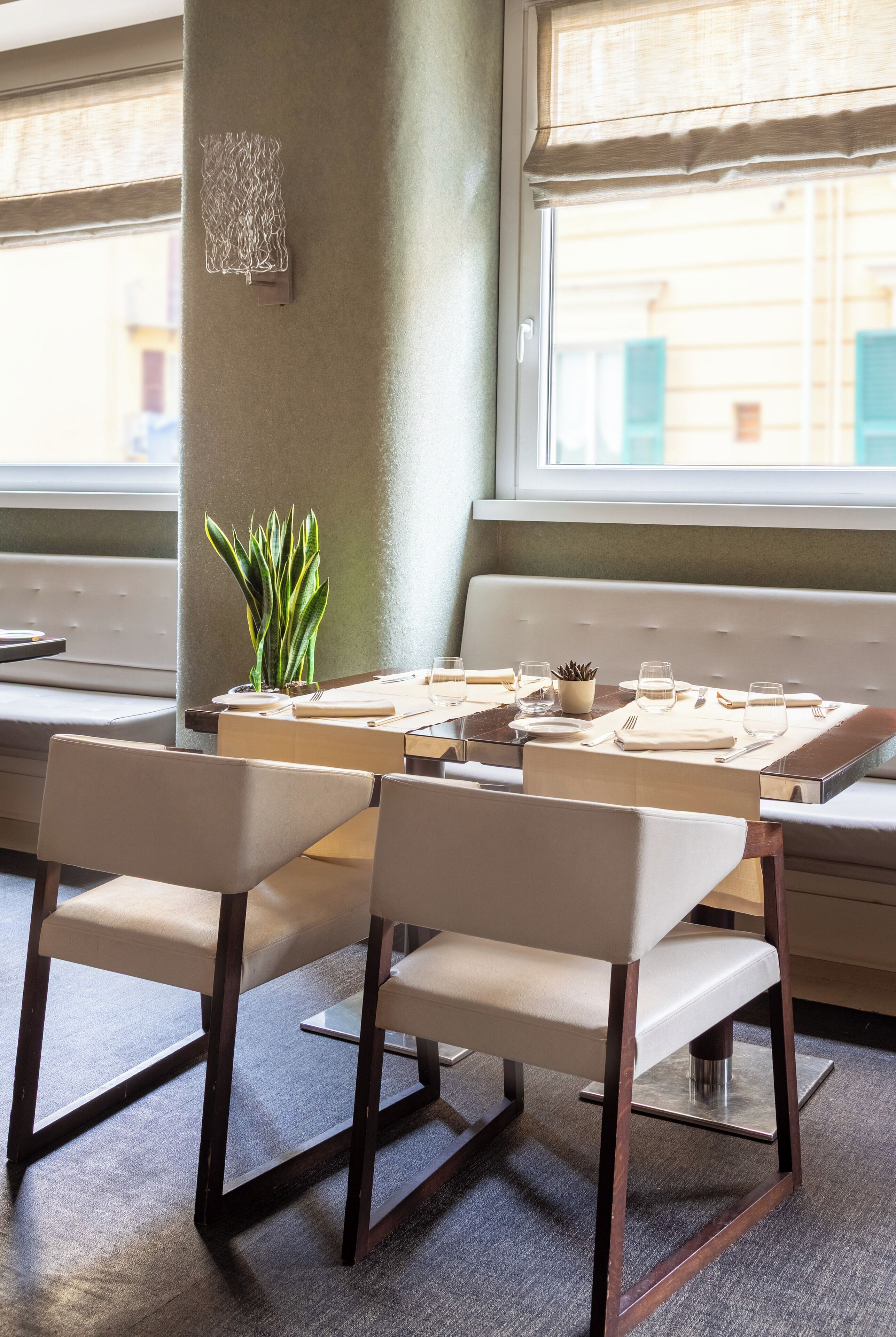 A dining area with a table set for two, a potted plant, and a window with a view of buildings.