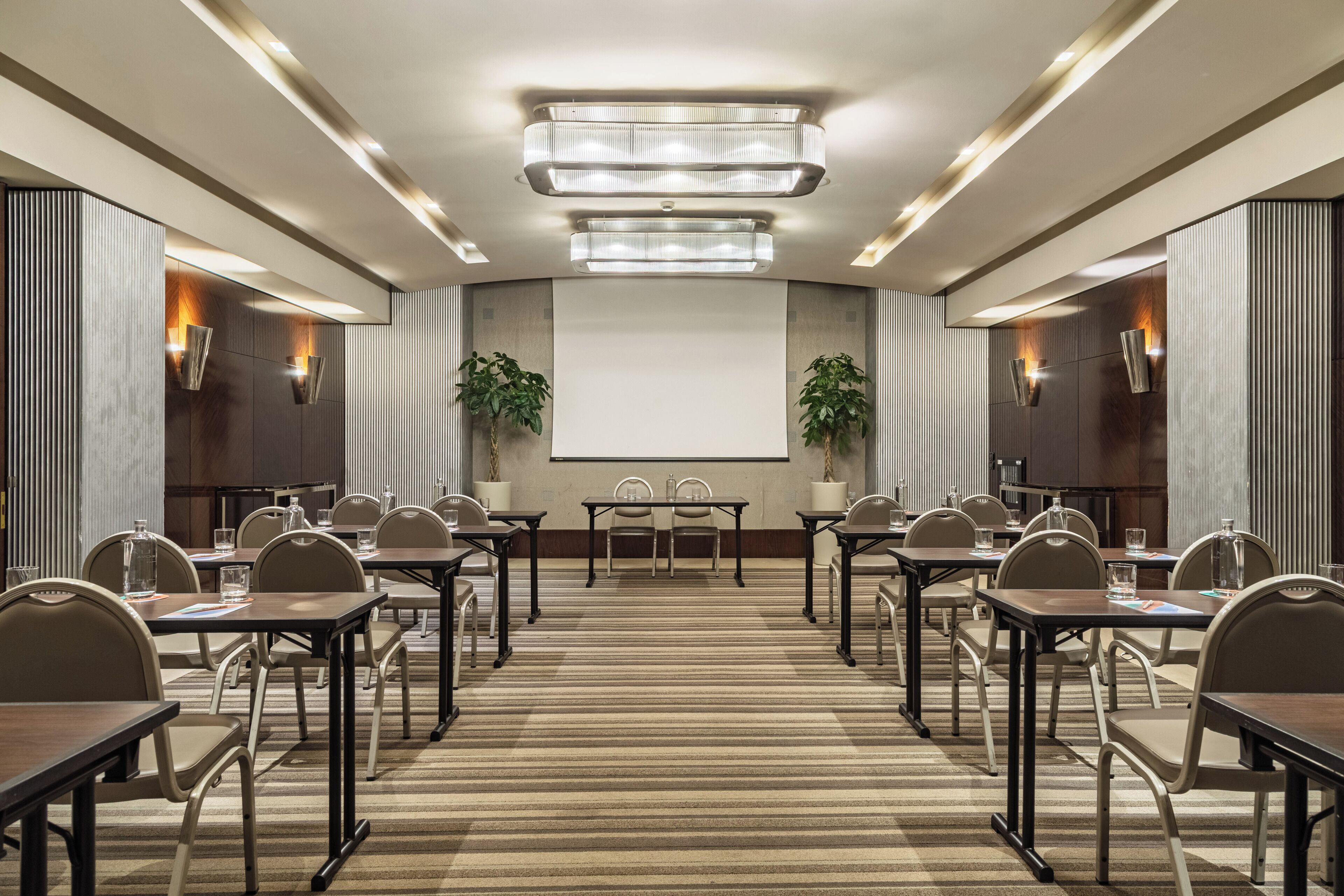 A conference room with a large screen, multiple tables, chairs, and ambient lighting.