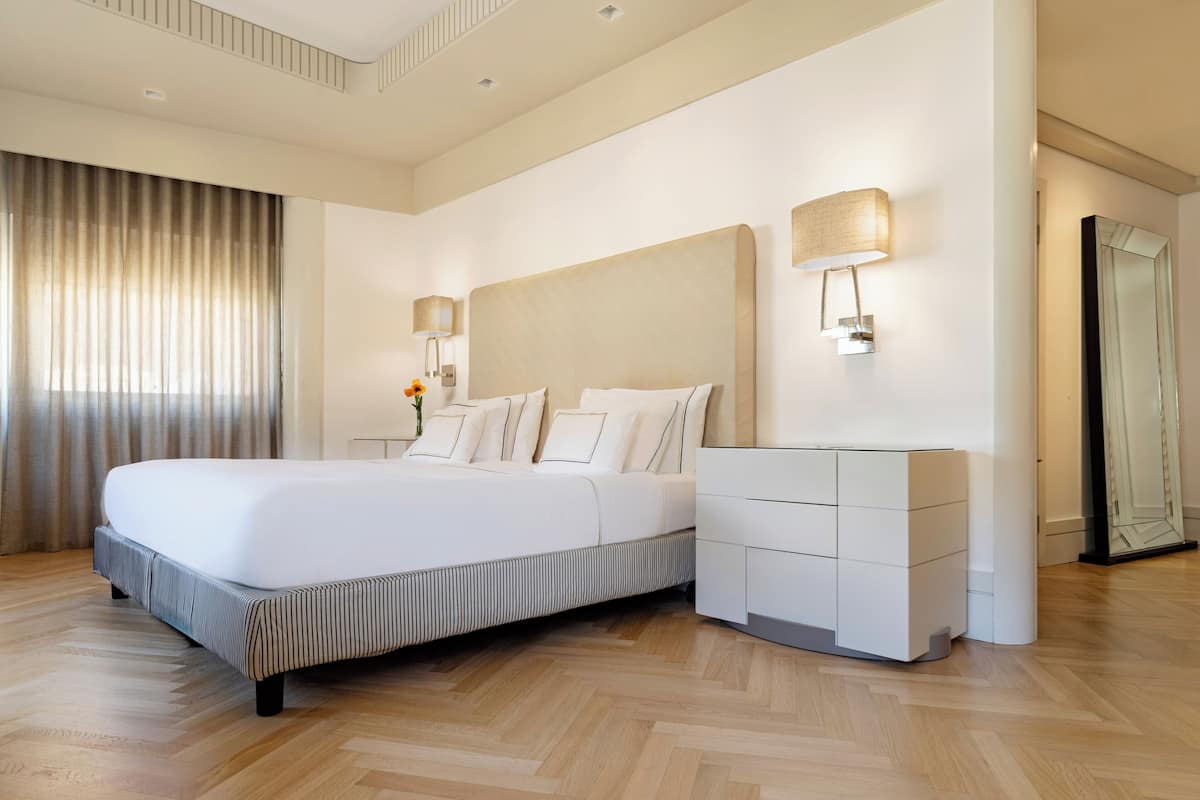 Ett modernt hotellrum med en stor säng, sänglampor, en byrå och en spegel.