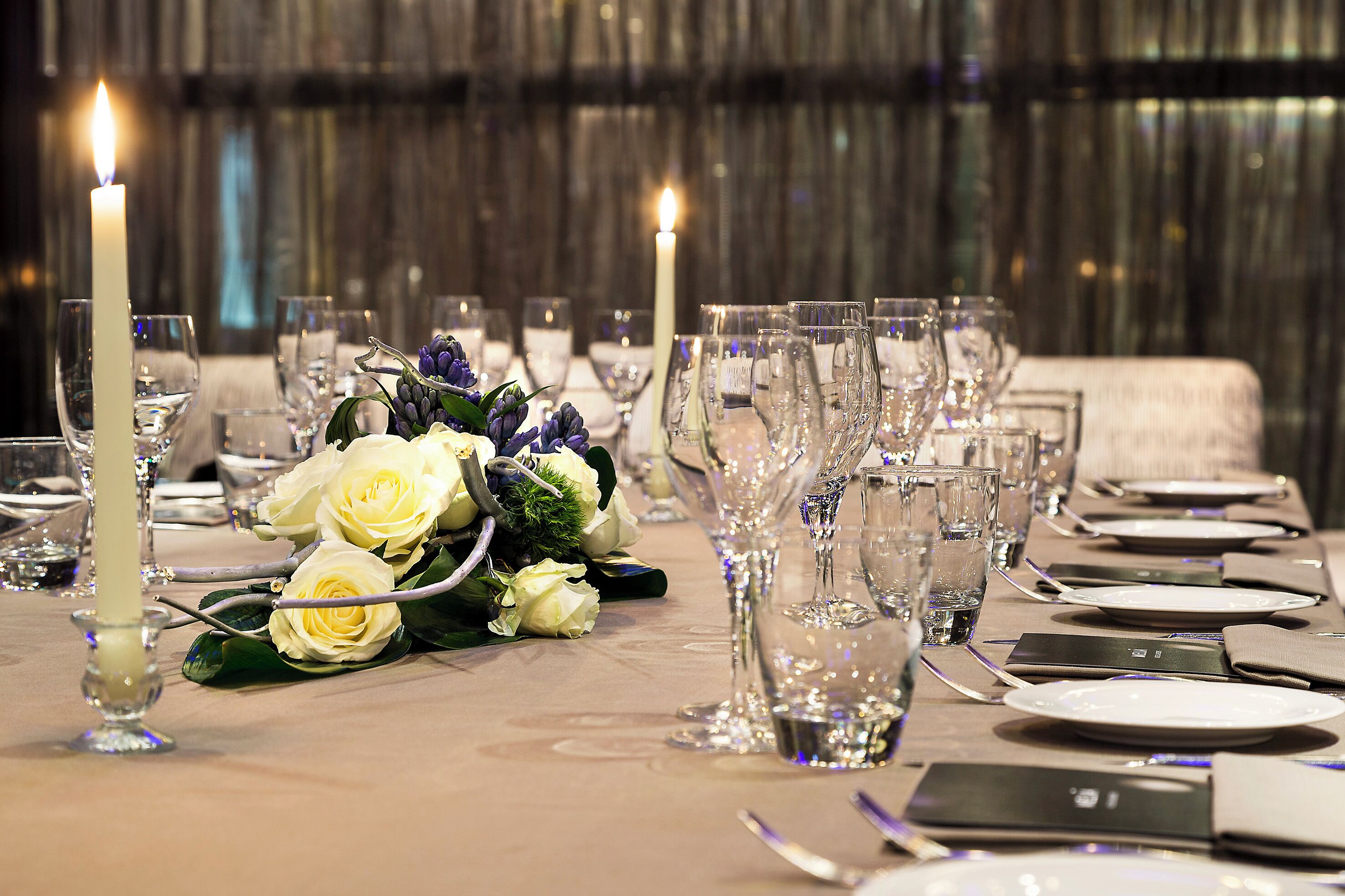Een gedekte tafel voor een formeel diner, compleet met kaarsen, glazen en een bloemstuk.