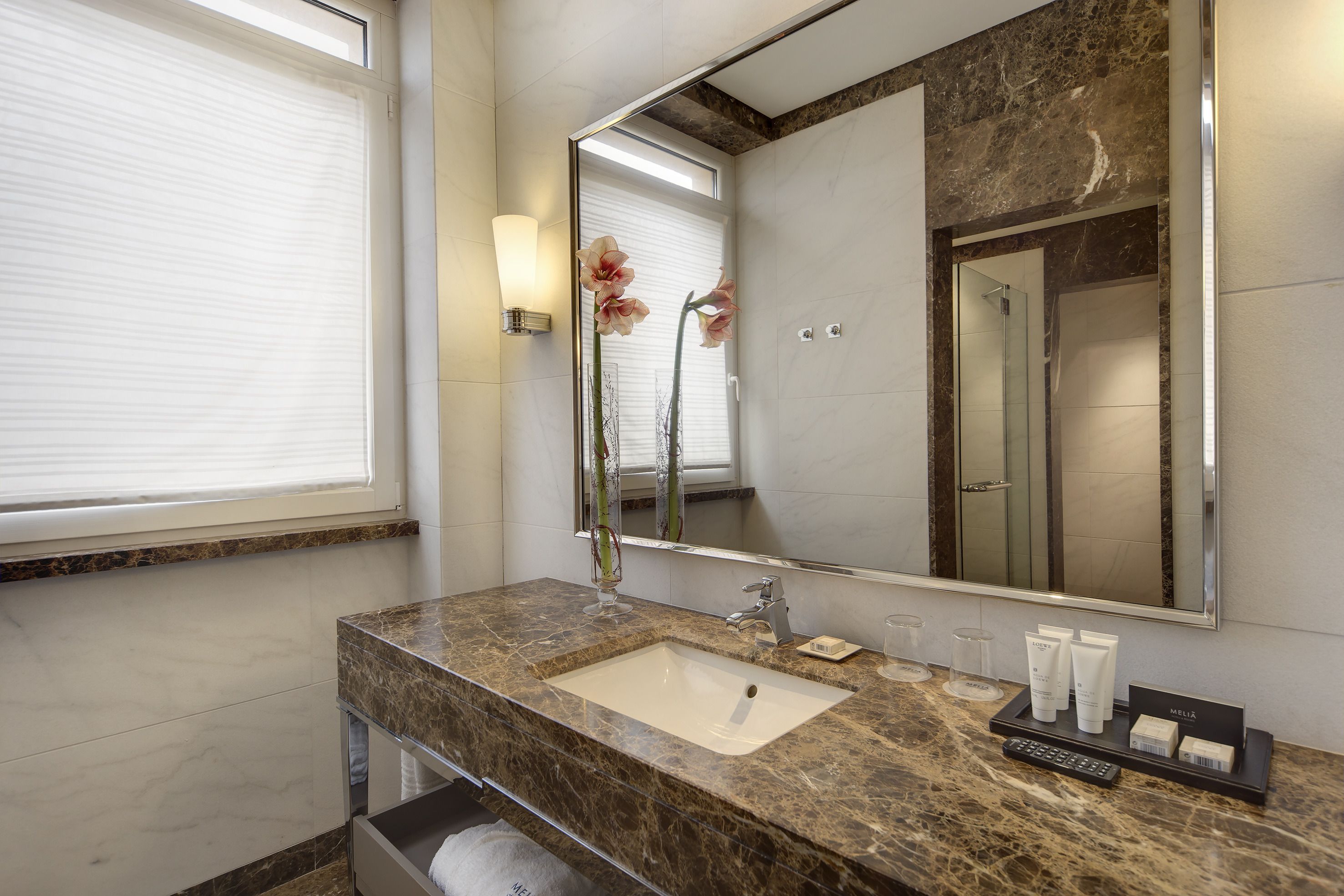 Un baño con un lavamanos de mármol, un espejo grande y un florero con flores.
