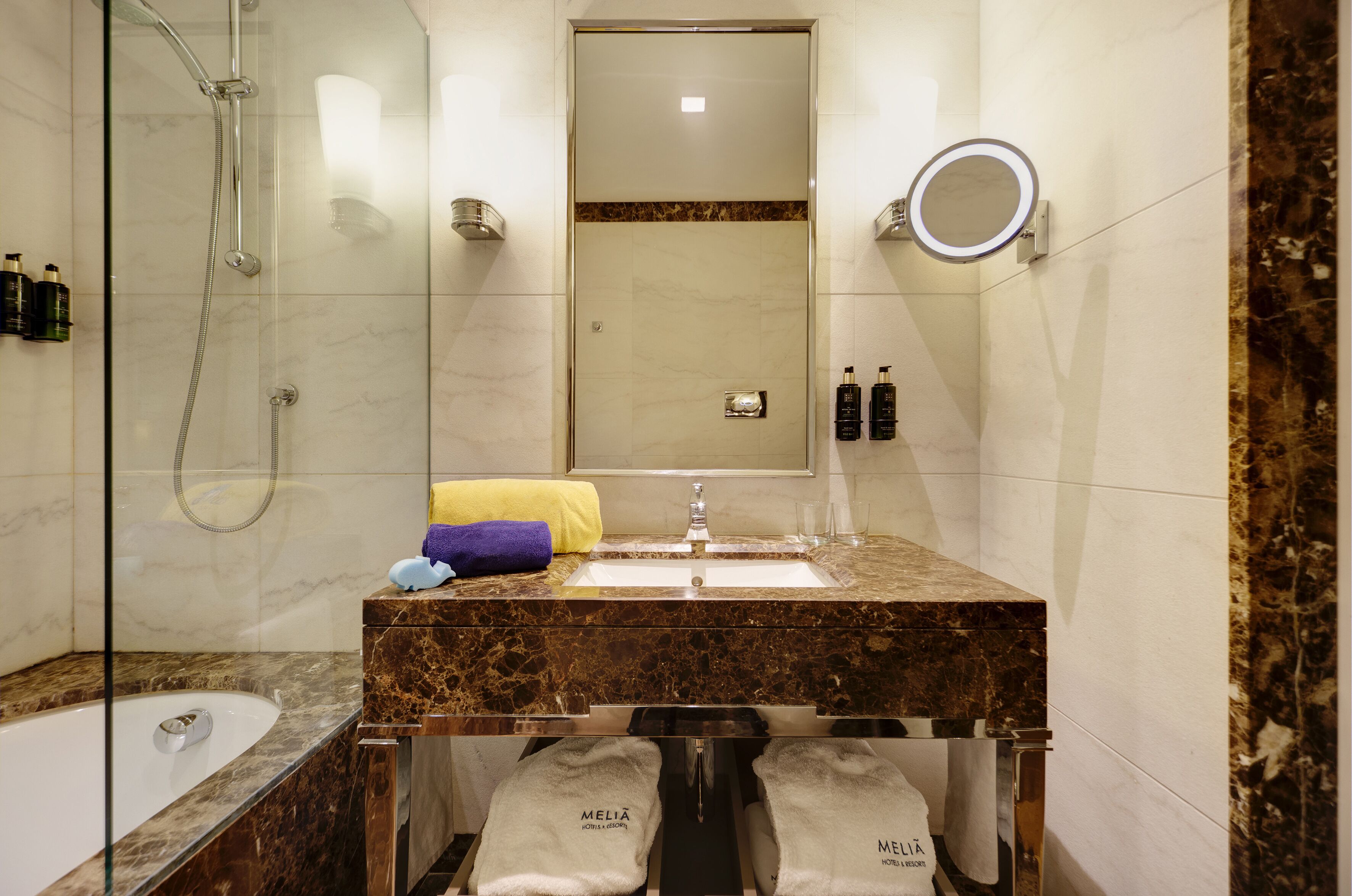 A modern bathroom with a glass-enclosed shower, a marble sink, and a large mirror.
