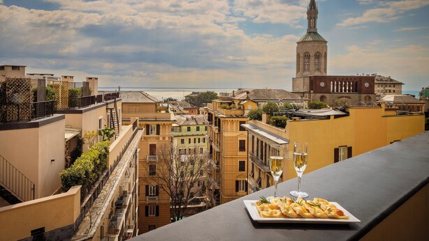 A terrace with a plate of food and a glass of wine, overlooking a cityscape with historic buildings and a church tower. - Melia Genova (Genoa)