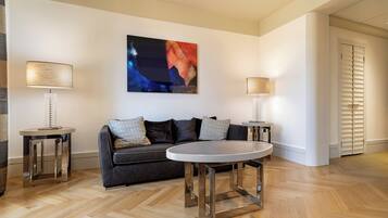 Una sala de estar moderna con un sofá gris oscuro, dos mesitas de noche con lámparas, una mesa redonda de centro y un cuadro abstracto grande en la pared.