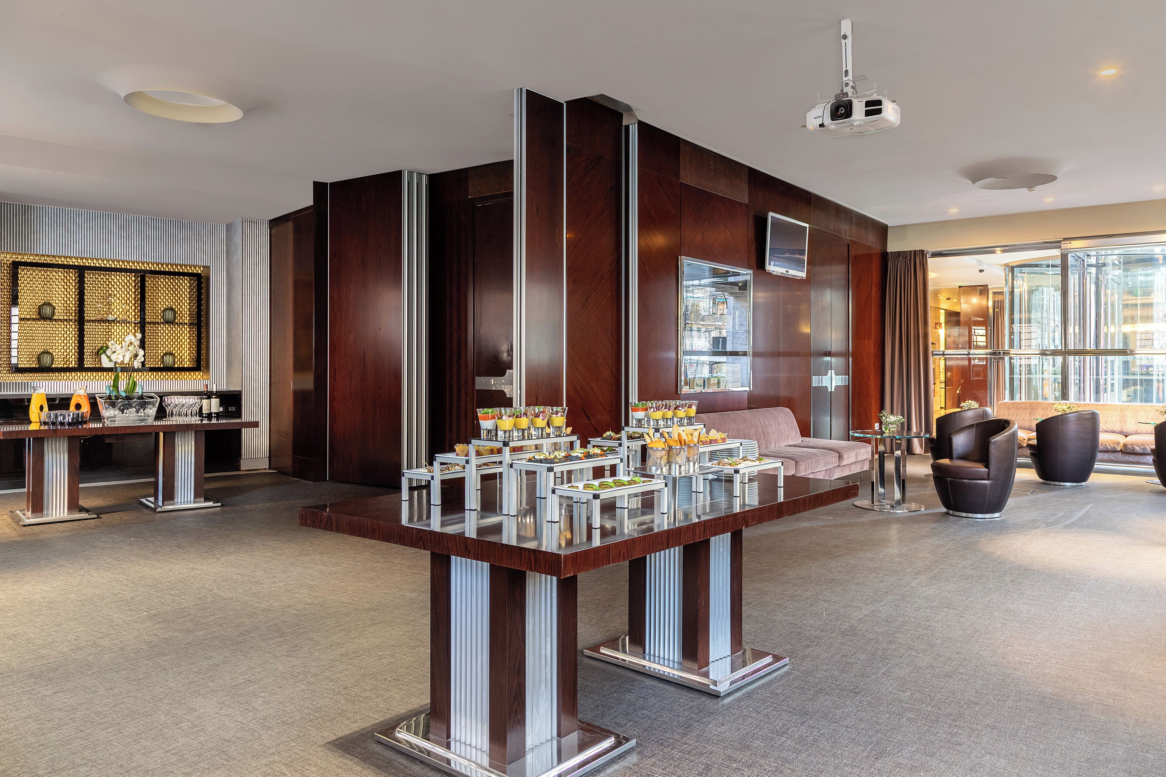 Una hall d'albergo moderna con un buffet centrale, zona salotto e ampie finestre.