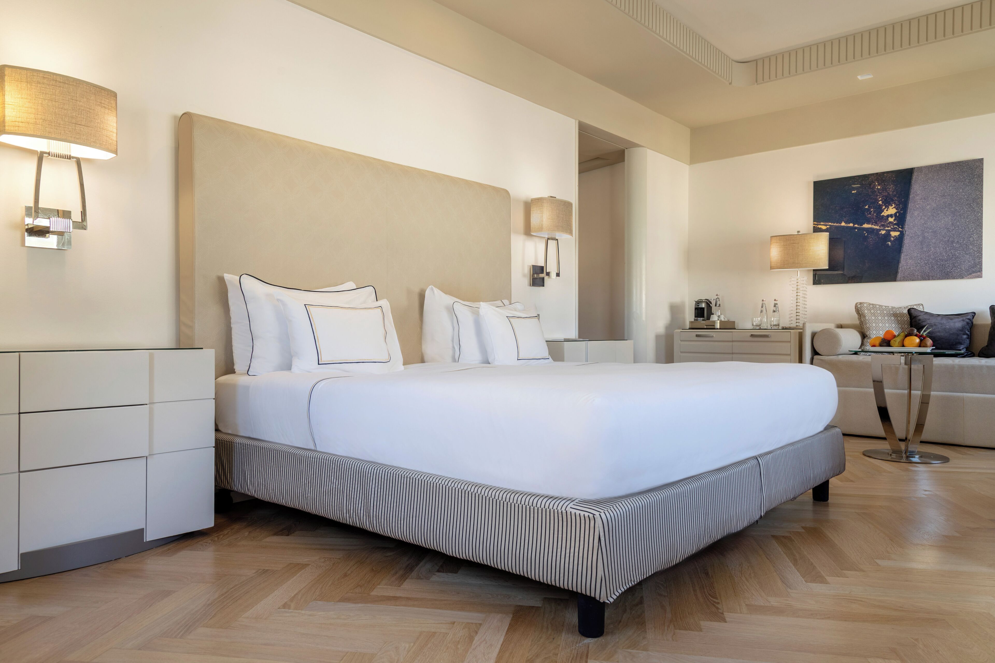 Una habitación de hotel moderna con una cama grande, mesitas de noche, un sofá y un cuadro en la pared.
