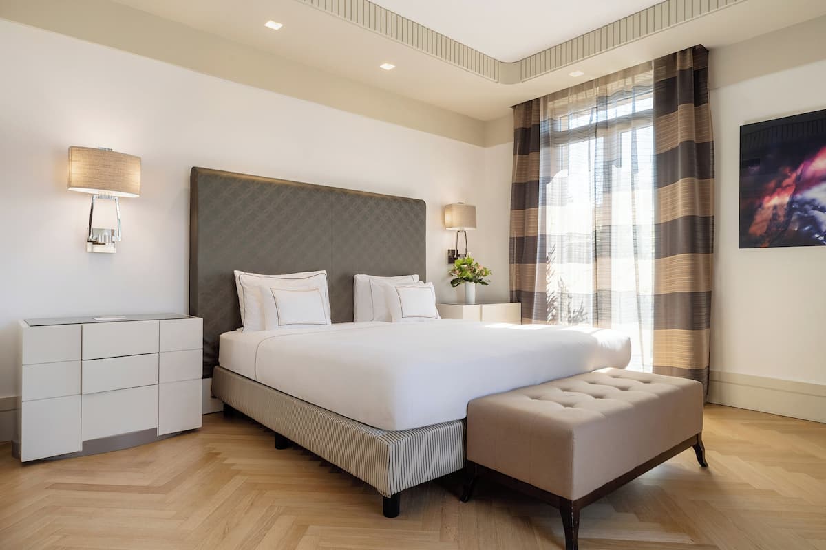 Ett modernt hotellrum med en stor säng, sänglampor, ett sängbord och utsikt över omgivningarna genom ett fönster med gardiner.