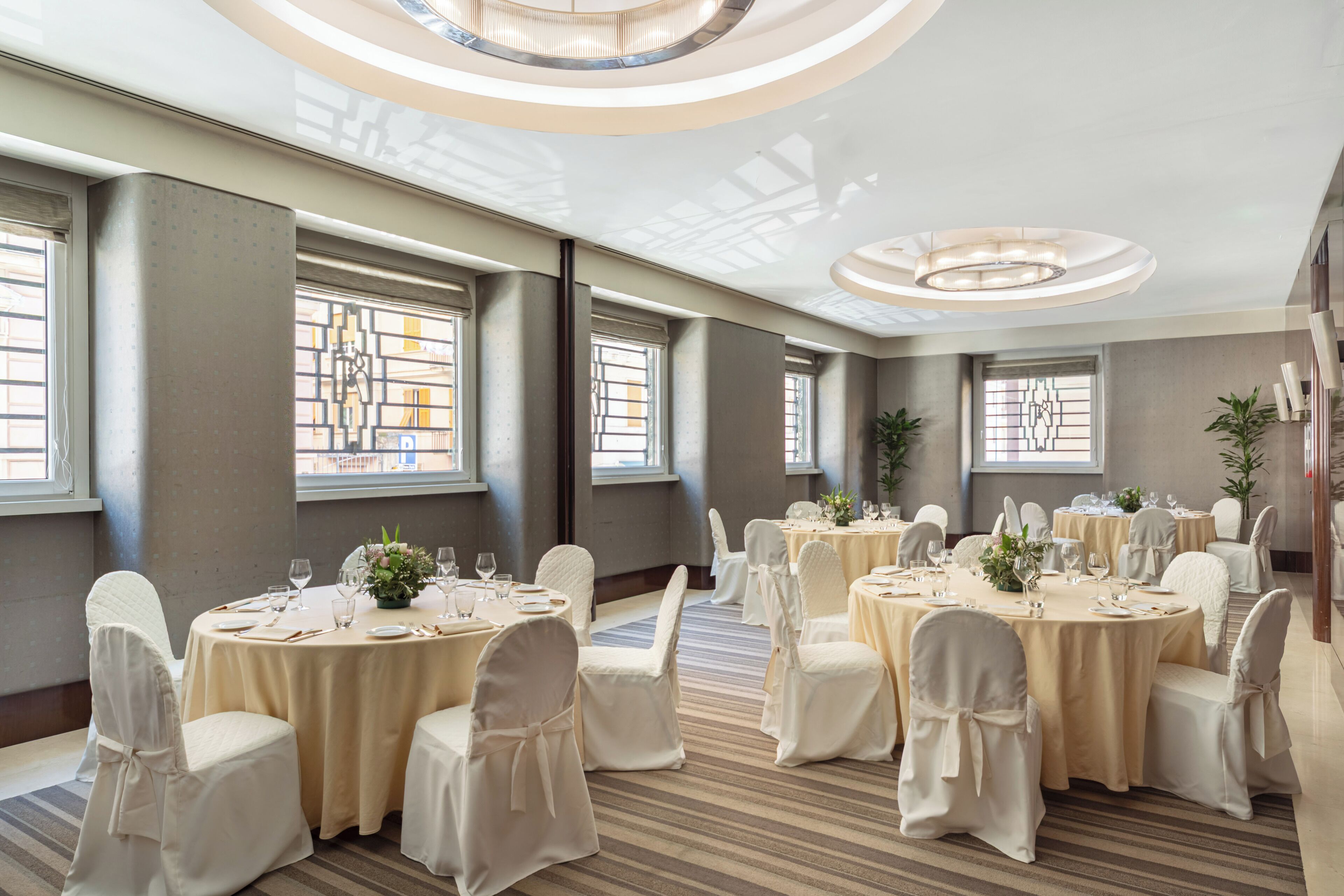 A banquet hall with round tables, white chairs, and chandeliers.