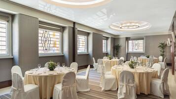 A banquet hall with round tables, white chairs, and chandeliers.