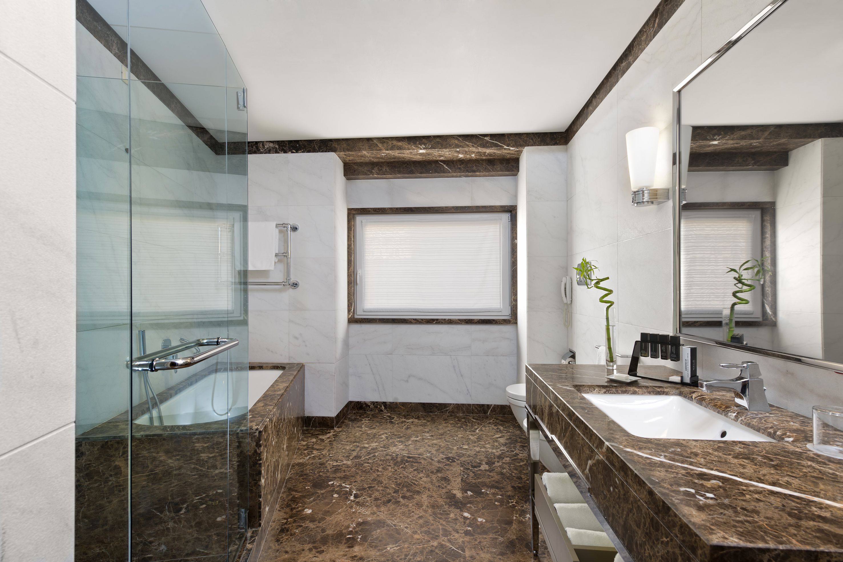 A modern bathroom with a glass shower enclosure, a marble-tiled floor, a sink with a marble countertop, and a large mirror.