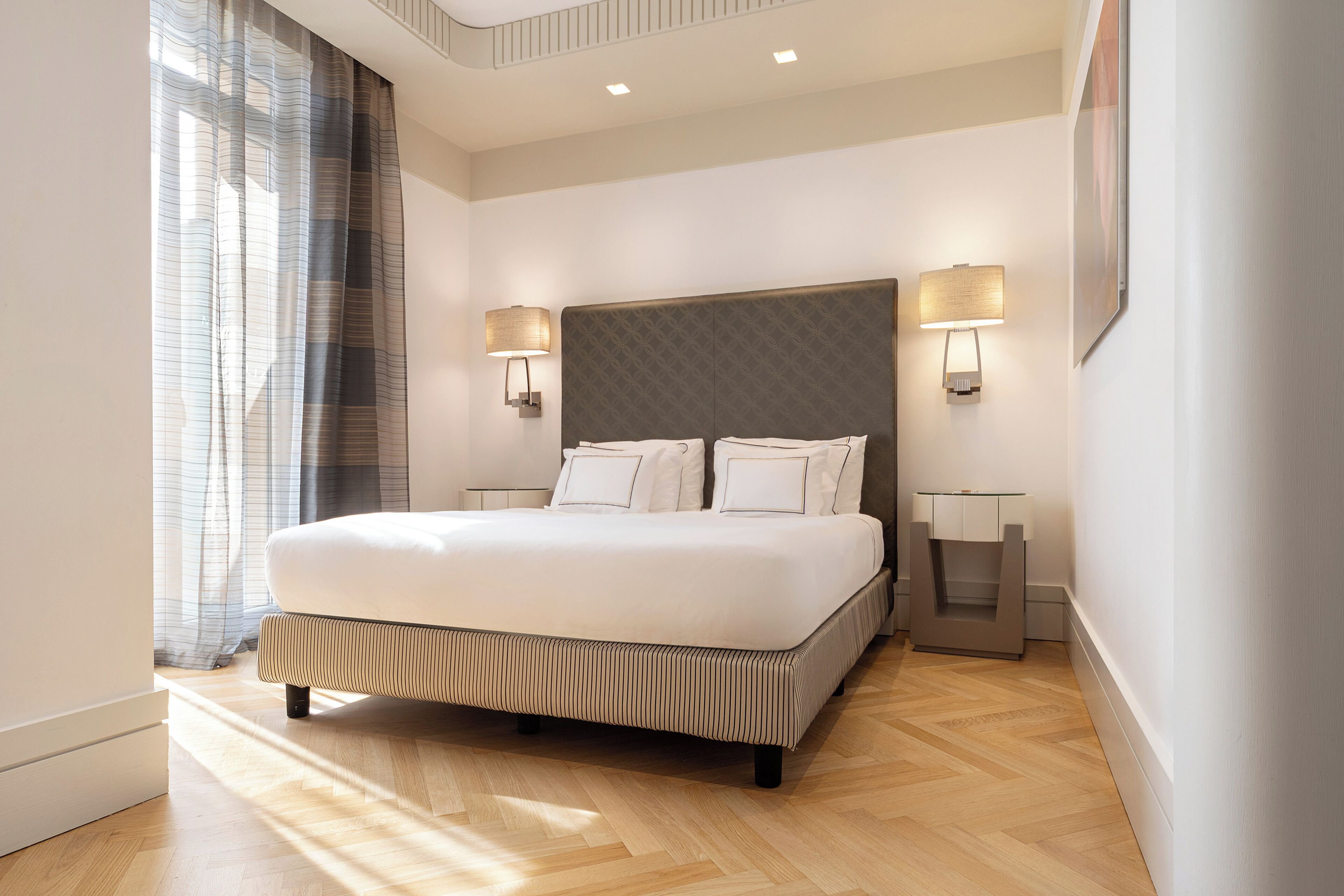 A modern hotel room with a large bed, two bedside tables, and a headboard with integrated lighting.