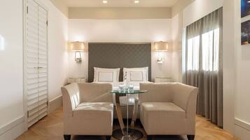 Quarto de hotel com uma cama, duas poltronas, uma mesa de vidro e um abajur.