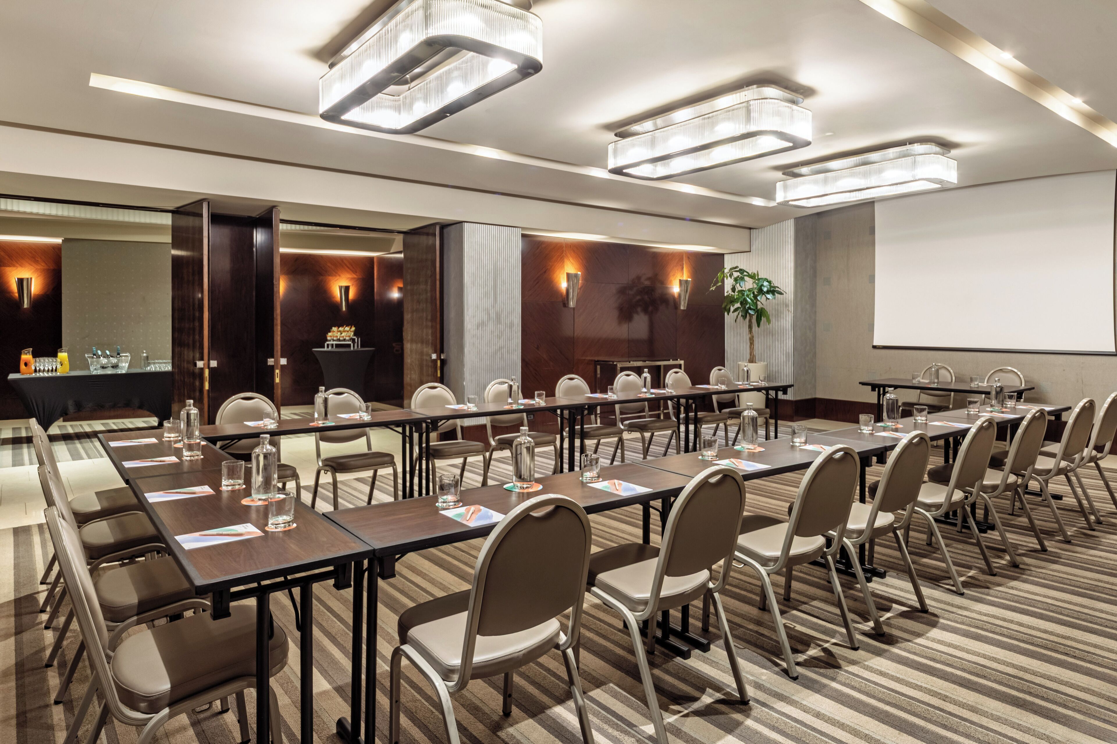 A conference room with long tables, chairs, and a projector screen.