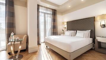 A modern hotel room with a large bed, a glass table, a chair, and a desk.