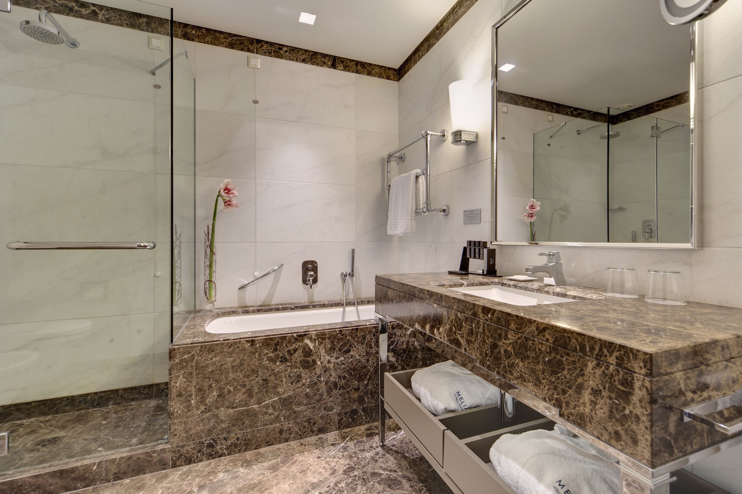 Un baño moderno con ducha de vidrio, tocador de mármol y un espejo grande.
