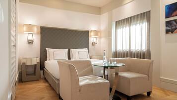 A hotel room with a bed, two armchairs, a glass table, a nightstand, and two wall-mounted lamps.