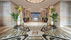 A modern hotel lobby with a geometric patterned floor, a central reception desk, and potted plants. - Melia Genova (Genoa)