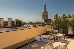 Een dakterras met een eettafel, omringd door rieten stoelen, met uitzicht op een stadsbeeld en een opvallende kerktoren.