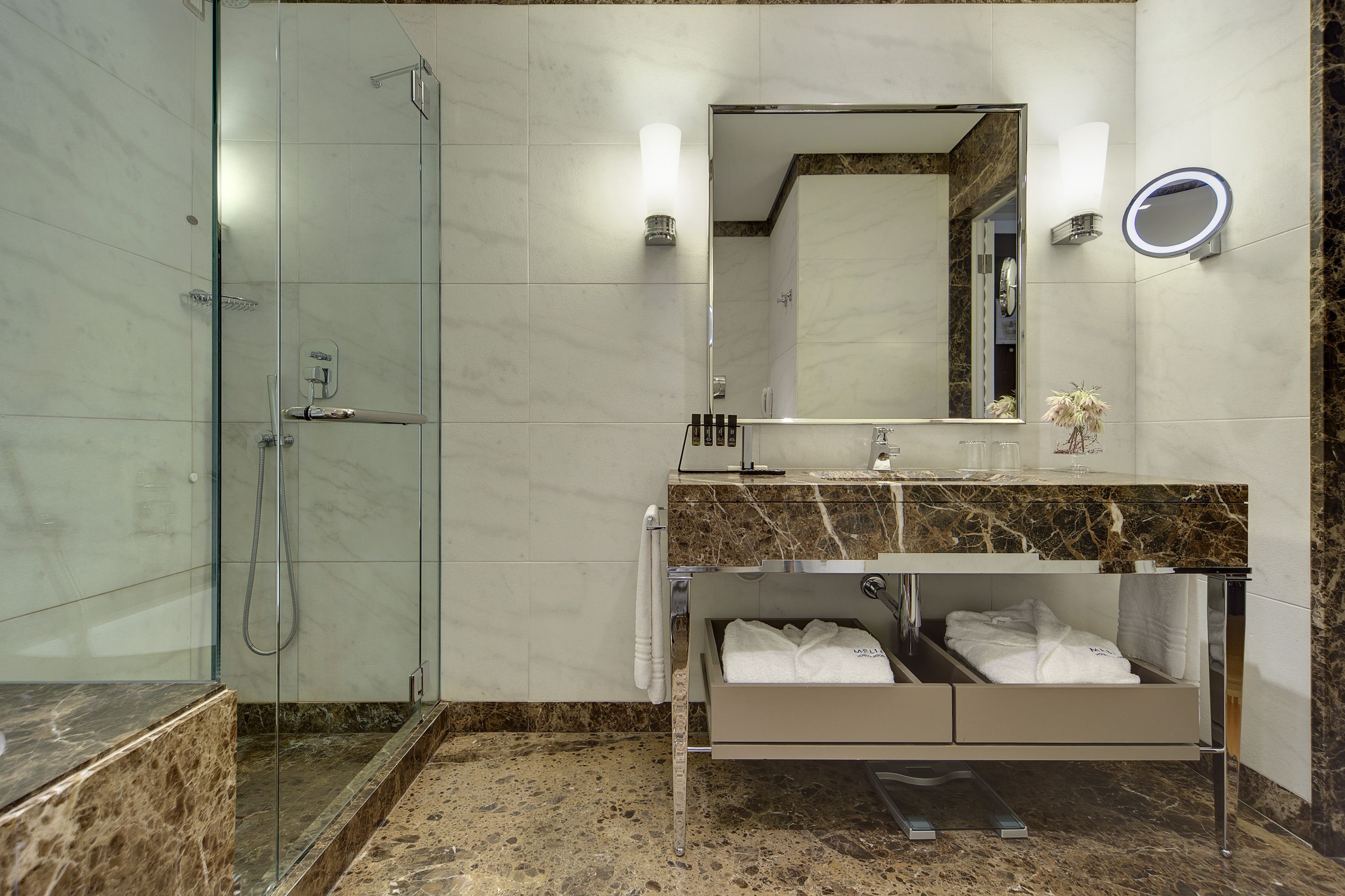 Une salle de bain moderne dotée d’une douche à parois de verre, d’un meuble-lavabo avec un plan de travail en marbre et d’un banc intégré où sont rangées les serviettes.