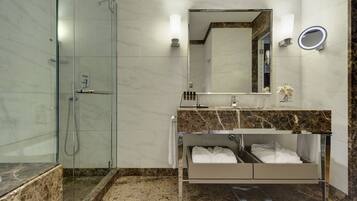 Une salle de bain moderne dotée d’une douche à parois de verre, d’un meuble-lavabo avec un plan de travail en marbre et d’un banc intégré où sont rangées les serviettes.