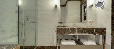 A modern bathroom with a glass-enclosed shower, a vanity with a marble countertop, and a built-in bench with towels.