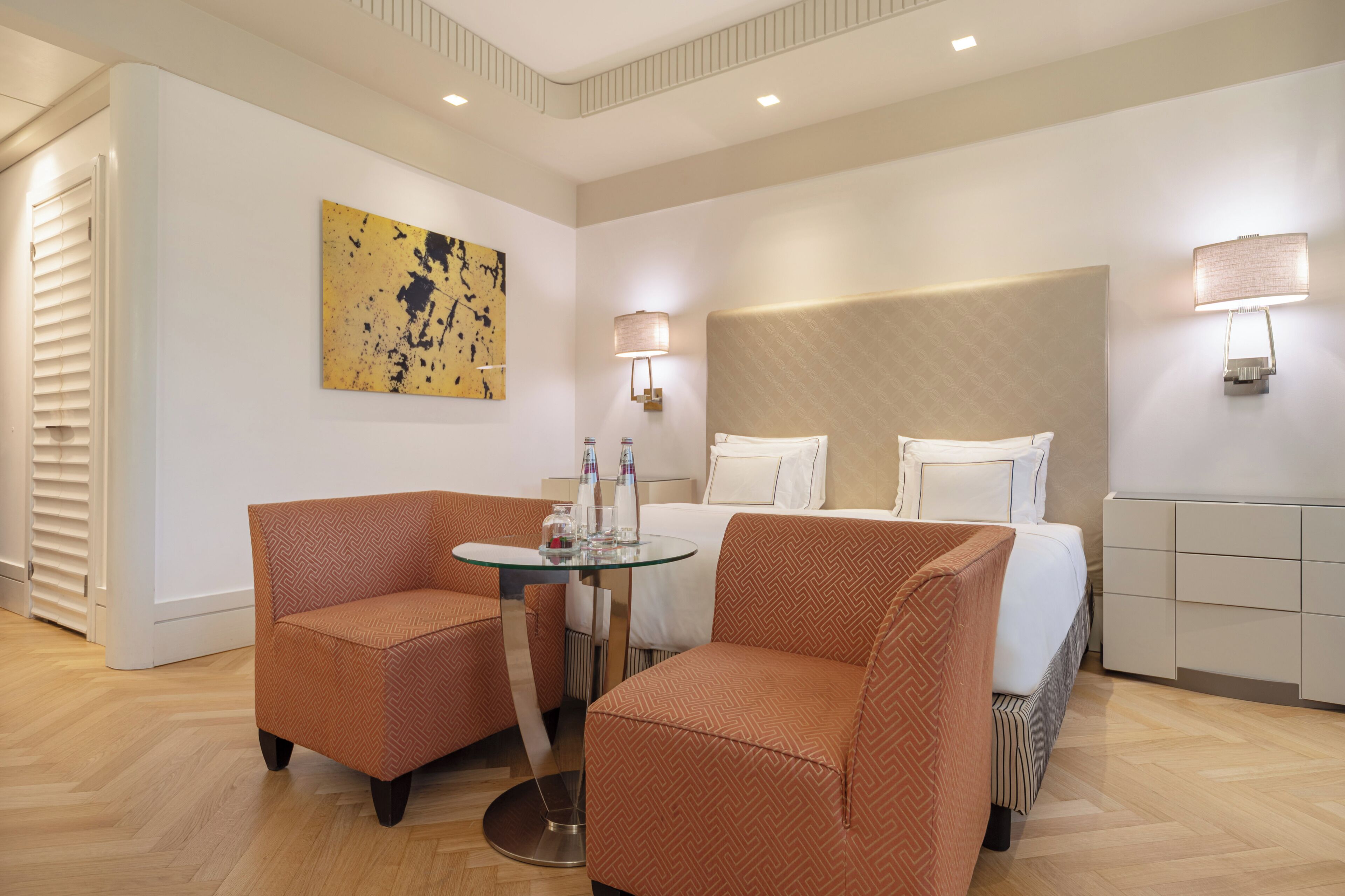 Ein Hotelzimmer mit Bett, zwei Sesseln, einem kleinen runden Tisch und einem Bild an der Wand.