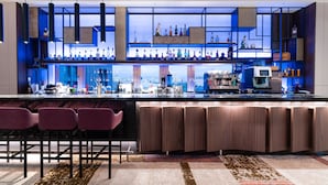 A modern bar area with a long counter, multiple shelves of bottles, and bar stools. - Howard Prince Hotel Taichung (Taichung)